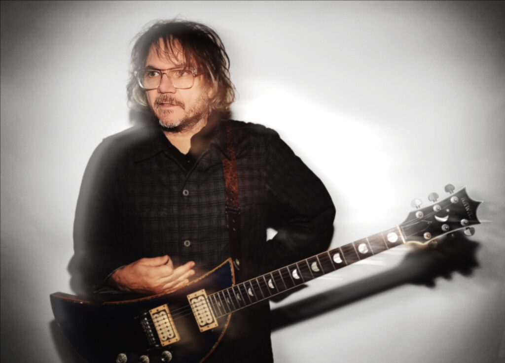 Jeff Tweedy posando con su guitarra, promocionando su álbum 'Twilight Override'.