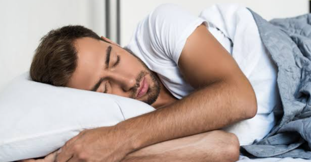 Persona durmiendo en una cama con un despertador al fondo
